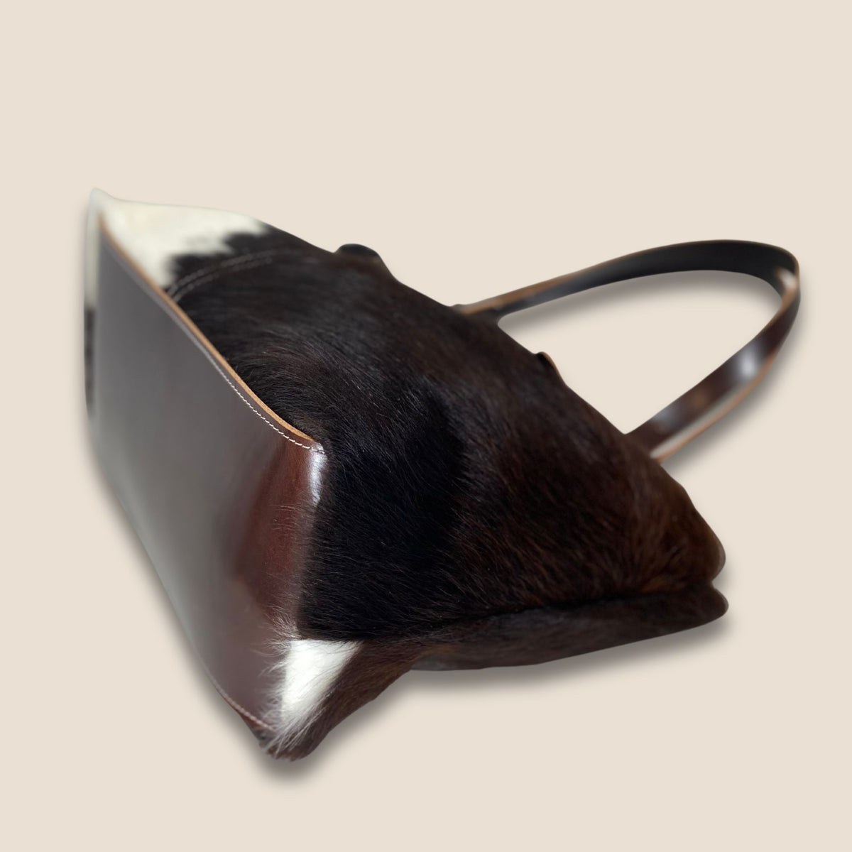 Fond en cuir marron du cabas Salers #27/160, avec couture périphérique et peau à poil naturel sur les côtés.