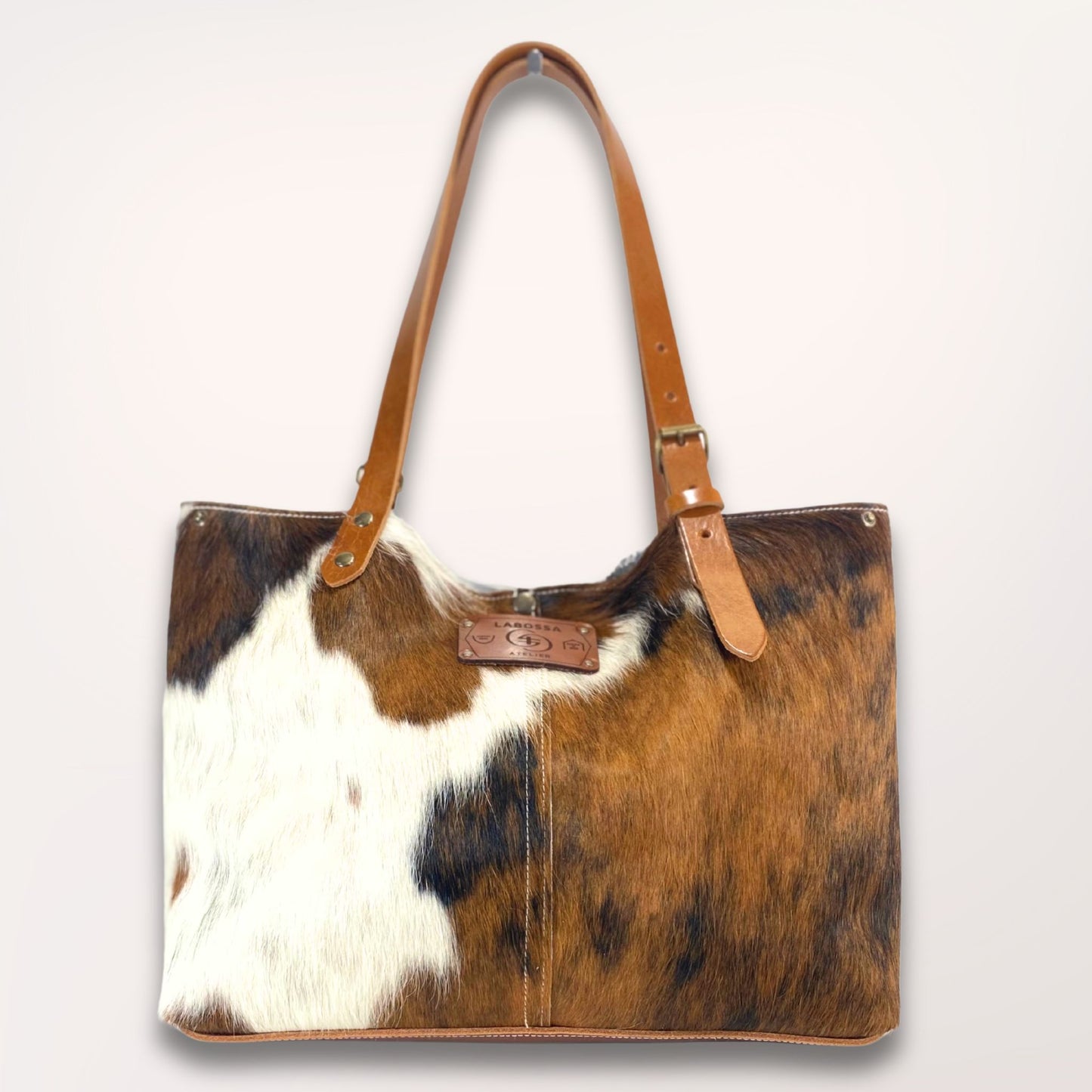 cabas peau de vache normande. Anse en cuir couleur cognac. Pris en studio sur fond clair.