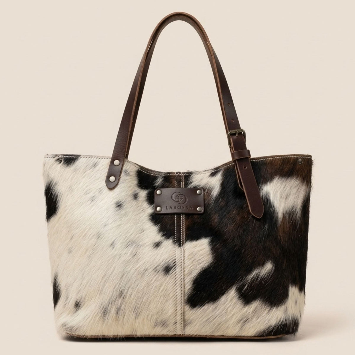 Cabas en peau de vache naturelle normande, robe noire, brune et blanche, anses en cuir marron et plaque Labossa sur le devant.