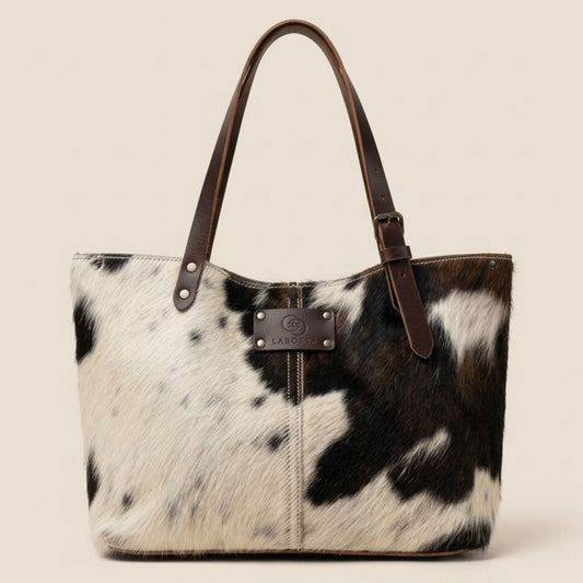 Cabas en peau de vache naturelle normande, robe noire, brune et blanche, anses en cuir marron et plaque Labossa sur le devant.