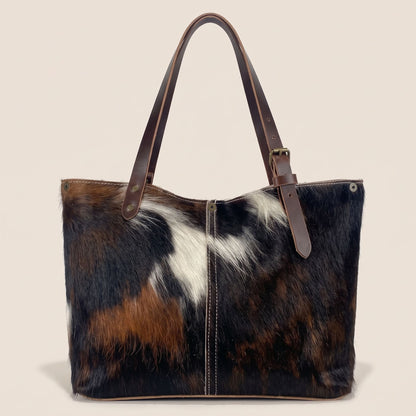 Dos du cabas en peau de vache normande, robe noire et brune, couture centrale contrastée et anses en cuir marron.