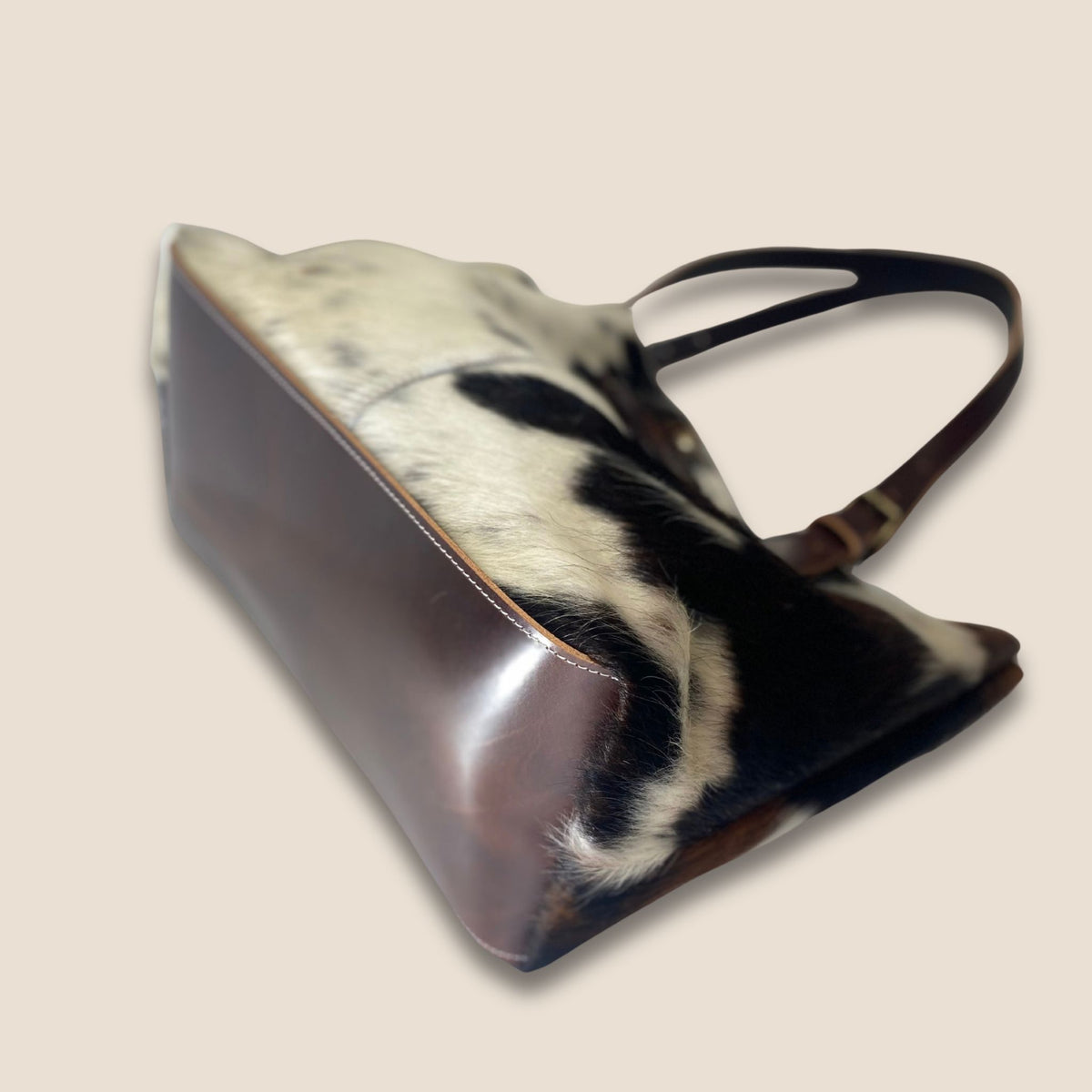 Fond du cabas en cuir marron avec couture périphérique, bordé de peau de vache naturelle noire et blanche.