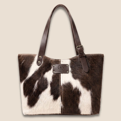 Cabas en peau de vache naturelle normande #27/150 vu de face, avec lanières en cuir marron chocolat et plaque Labossa.