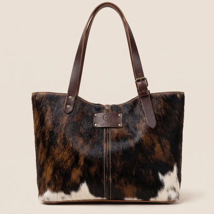 Cabas en peau de vache naturelle normande #27/159, robe noire, brune et blanche, avec anses en cuir marron.