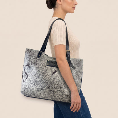 Cabas en peau de vache naturelle Vosgienne porté à l’épaule par un modèle, avec lanières en cuir noir.