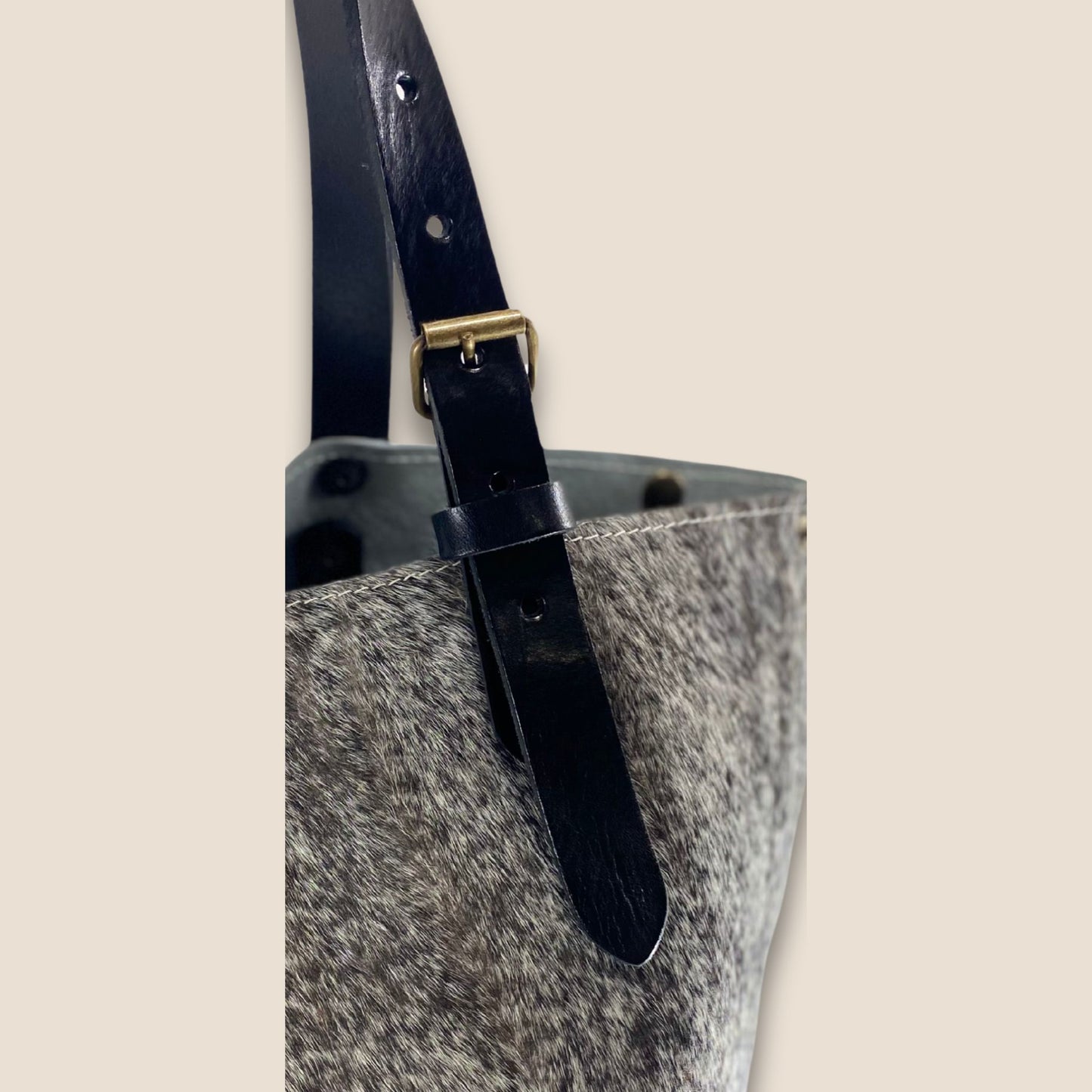 Gros plan des lanières en cuir noir du cabas, avec boucle métallique, trous de réglage et rivets.
