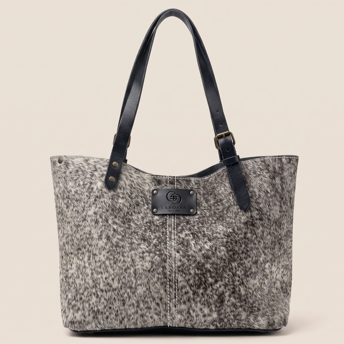 Cabas en peau de vache naturelle Vosgienne blanche mouchetée, vue de face, avec lanières en cuir noir et patch Labossa.