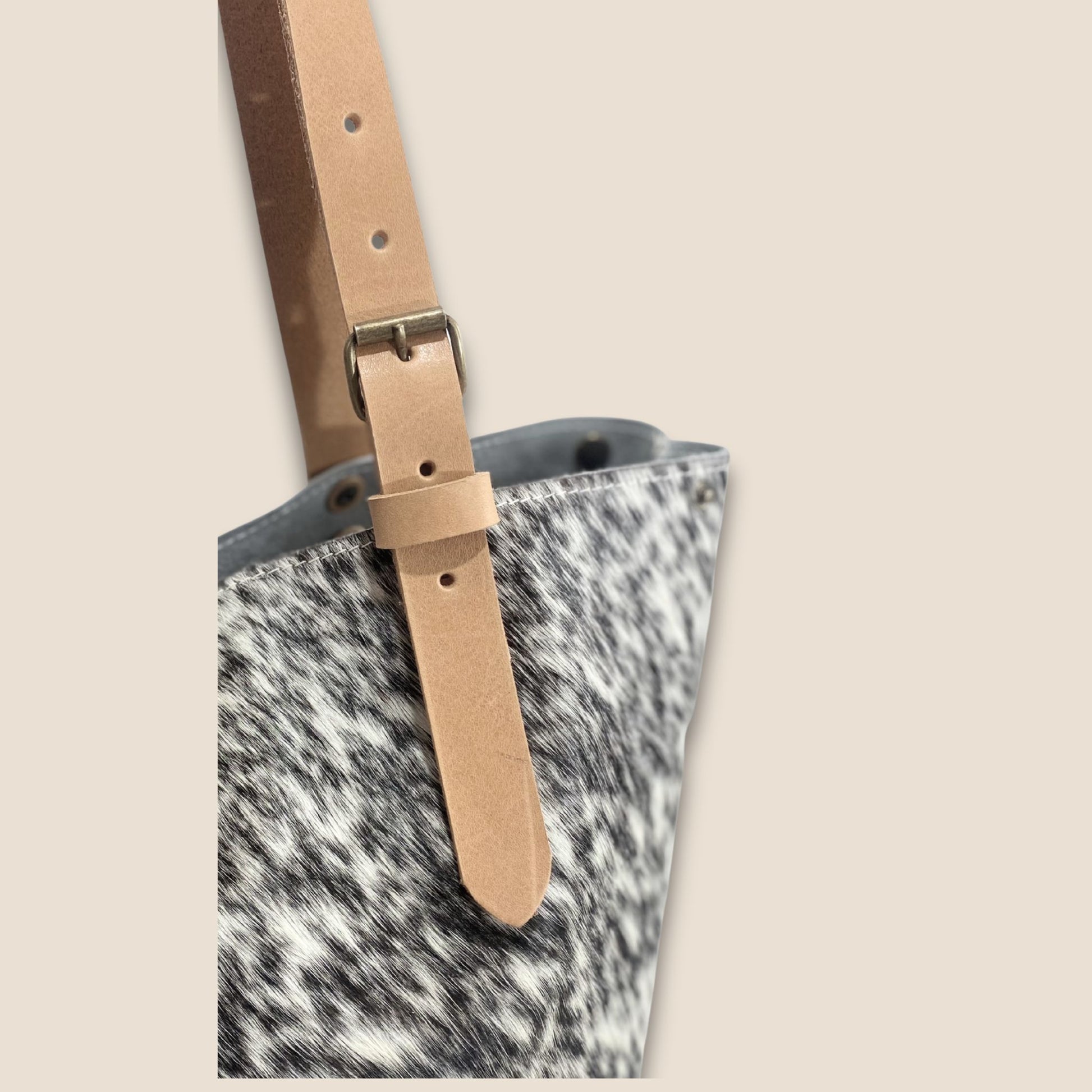 Gros plan sur la lanière réglable en cuir cognac, sa boucle et ses rivets.