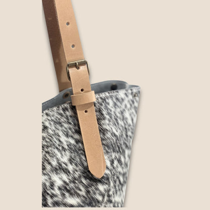 Gros plan sur la lanière réglable en cuir cognac, sa boucle et ses rivets.