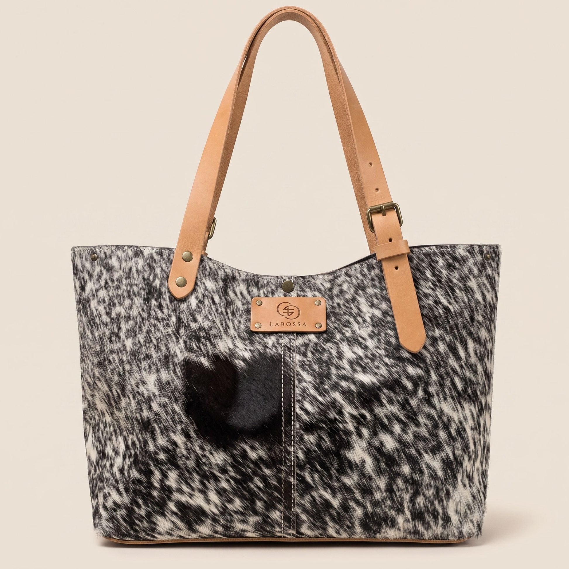 Cabas en peau de vache naturelle Vosgienne #13/149 vu de face, avec robe noire et blanche mouchetée, lanières en cuir cognac et plaque Labossa.