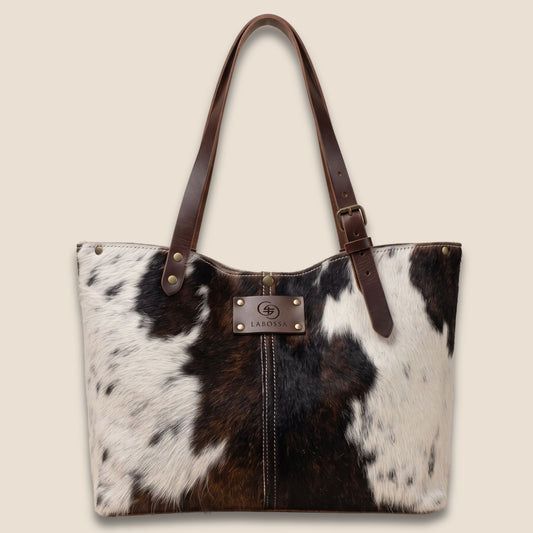 Cabas en peau de vache naturelle blanche, brune et noire, avec anses en cuir marron et patch Labossa.