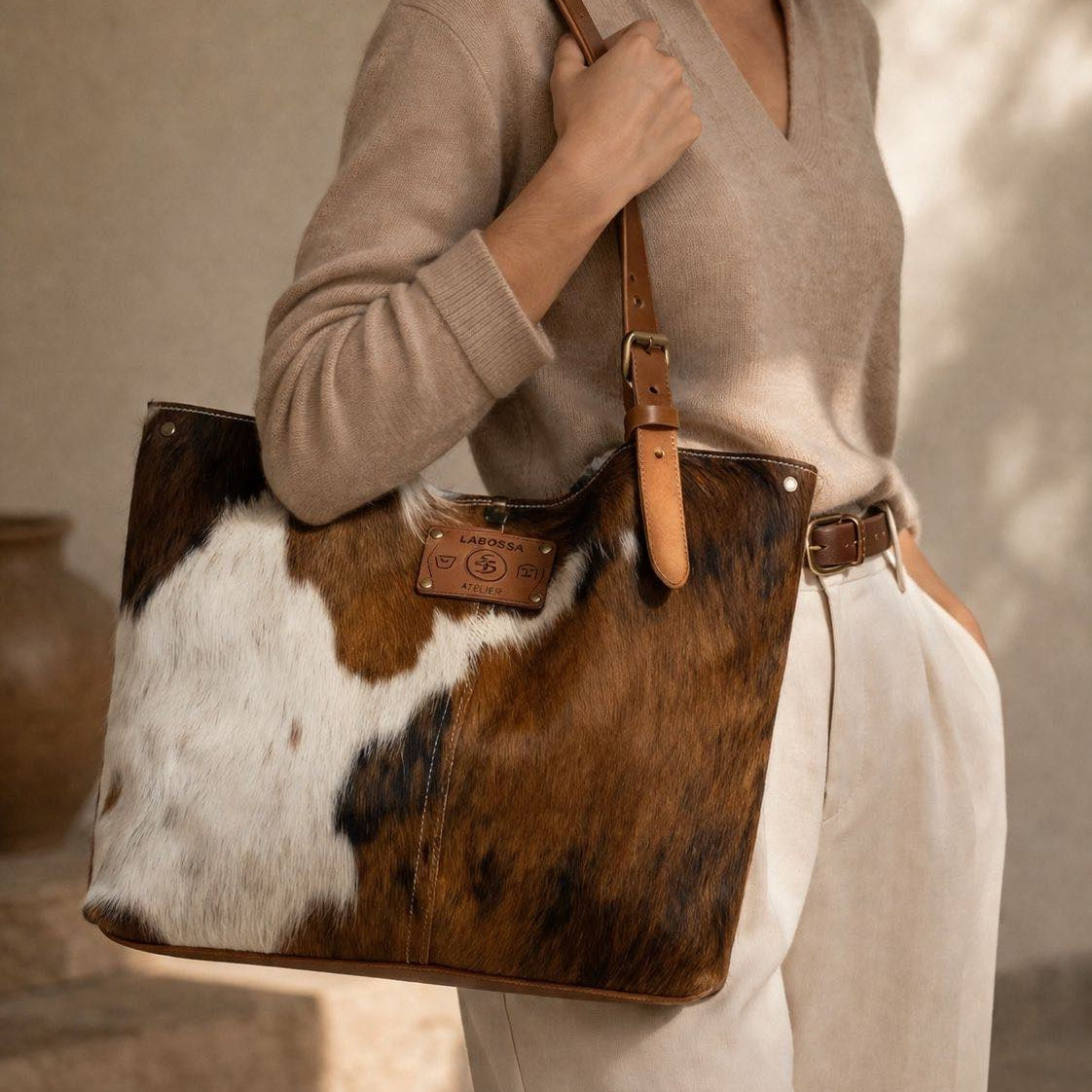 Cabas artisanal Labossa modèle 27111 en peau de vache normande aux motifs naturels marron et blanc, équipé d'anses en cuir robuste et d'une plaque logo en cuir.  modèle chic studio.