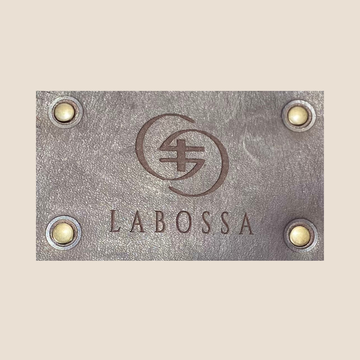 Gros plan du patch extérieur en cuir lisse Primavera marron, gravé du logo Labossa et fixé par quatre rivets.
