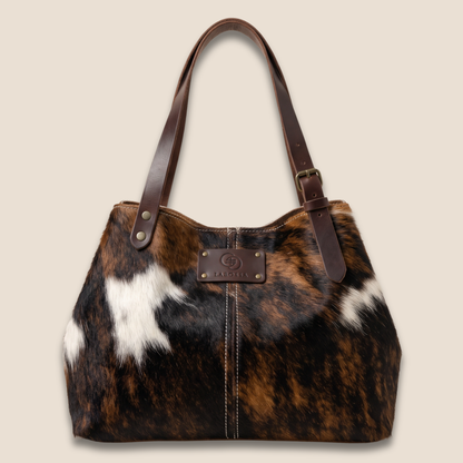 Cabas en peau de vache normande vu de face, côtés resserrés, avec patch Labossa et lanières marron à boucles.