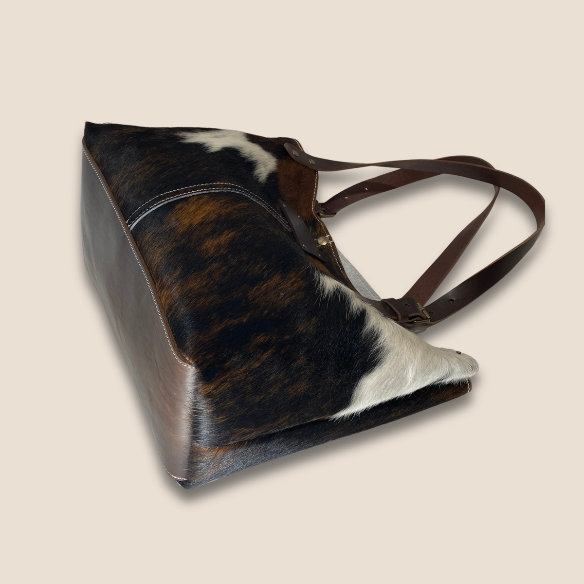  Vue du dessous du cabas, montrant le fond en cuir marron lisse, sa couture périphérique et les côtés en peau naturelle.