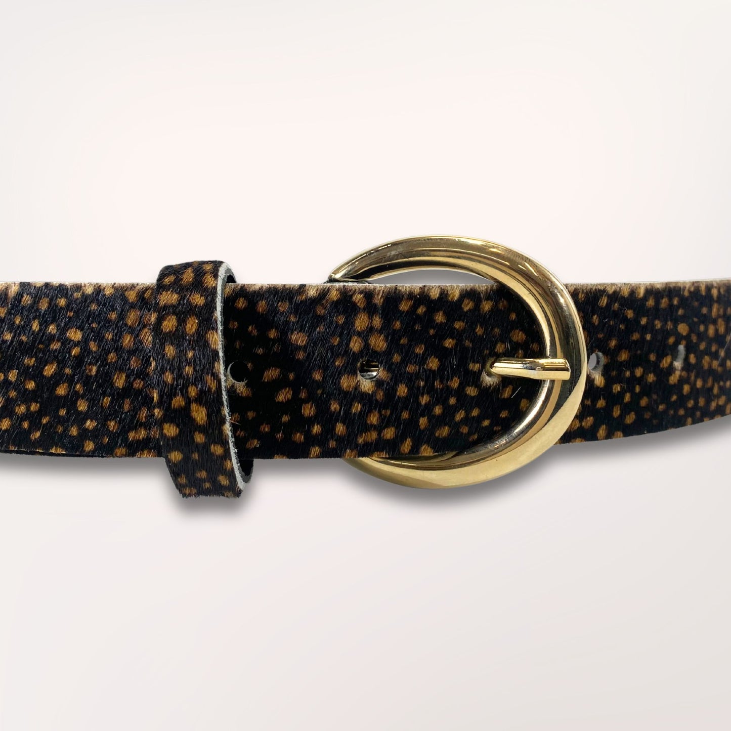 Gros plan sur la boucle dorée et la texture riche du cuir poil de vache au motif léopard de la ceinture Savana, maroquinerie de qualité faite main.