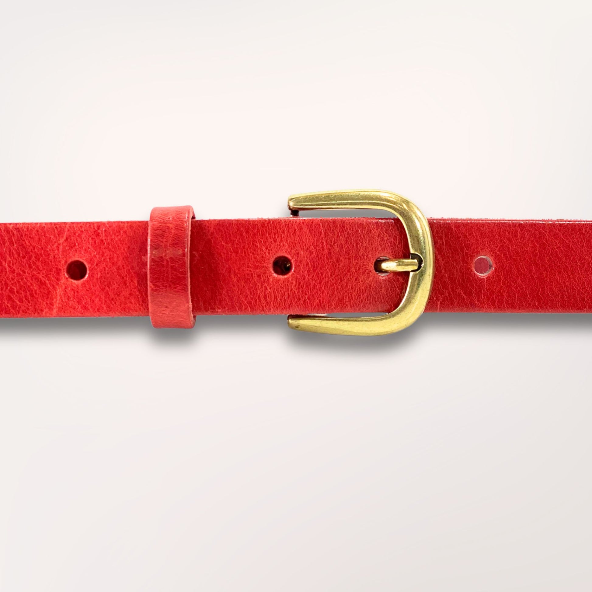Détail de la boucle dorée et du grain de cuir rouge, ceinture artisanale durable.