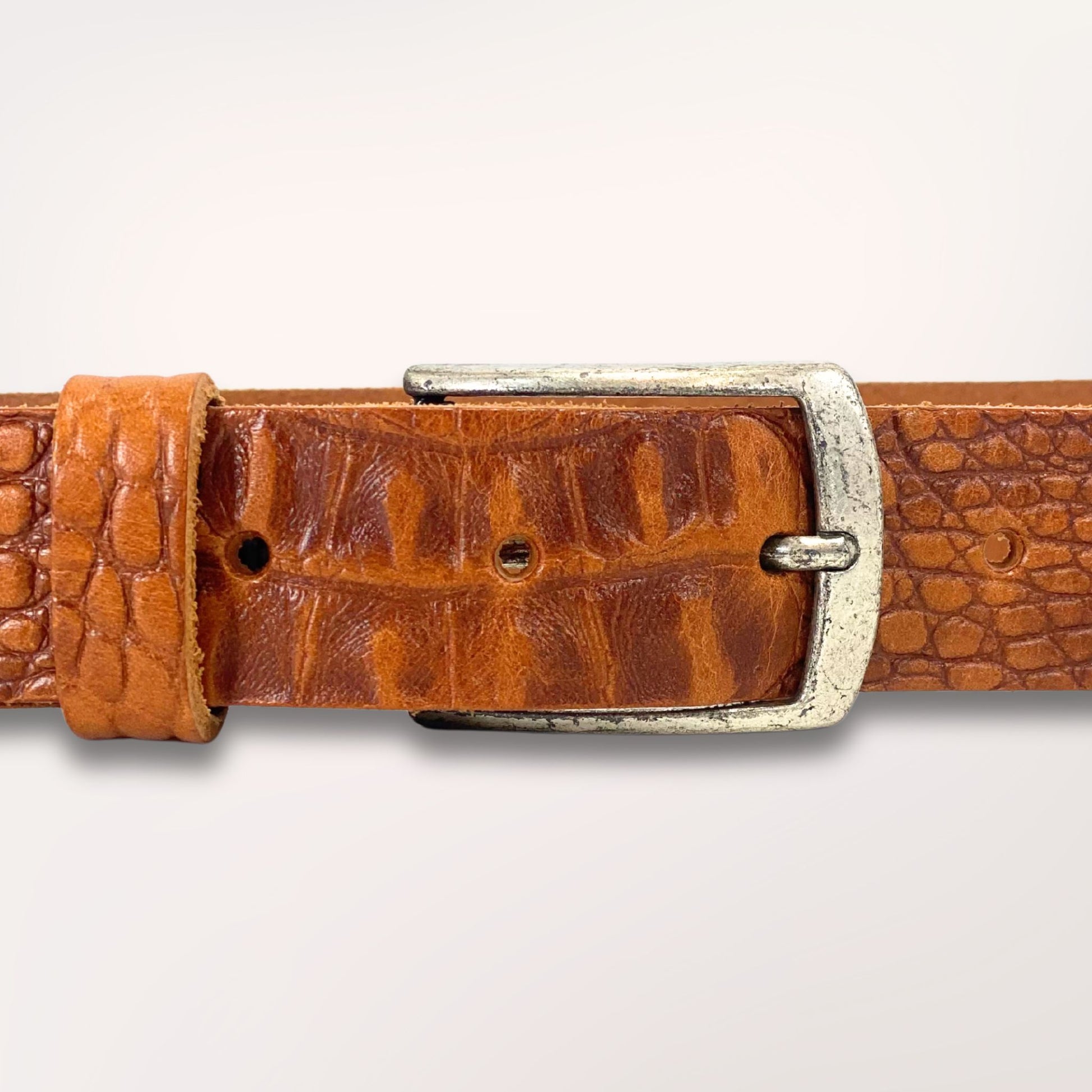 Gros plan sur la texture cuir cognac embossé caïman et la boucle de la ceinture Primavera, finition artisanale Labossa.