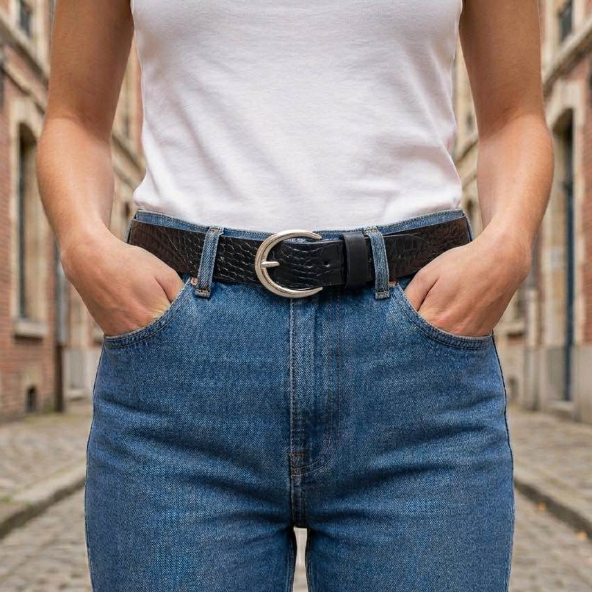 Ceinture en cuir noir motif caïman portée sur un jean bleu, look sophistiqué et intemporel, fabrication française.