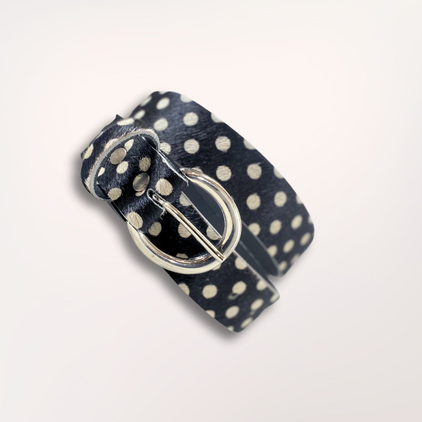 Ceinture artisanale Swing Labossa en cuir de vachette à poil court imprimé pois noirs, enroulée pour souligner la souplesse du cuir et la finition de la boucle argentée brossée.