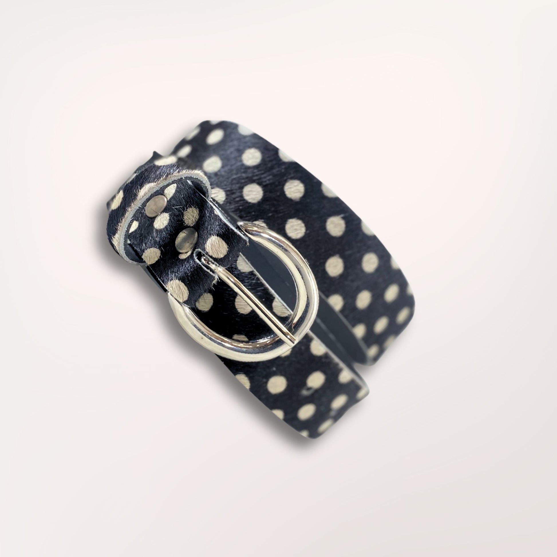 Ceinture artisanale Swing Labossa en cuir de vachette à poil court imprimé pois noirs, enroulée pour souligner la souplesse du cuir et la finition de la boucle argentée brossée.