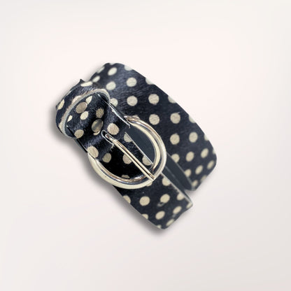 Ceinture artisanale Swing Labossa en cuir de vachette à poil court imprimé pois noirs, enroulée pour souligner la souplesse du cuir et la finition de la boucle argentée brossée.