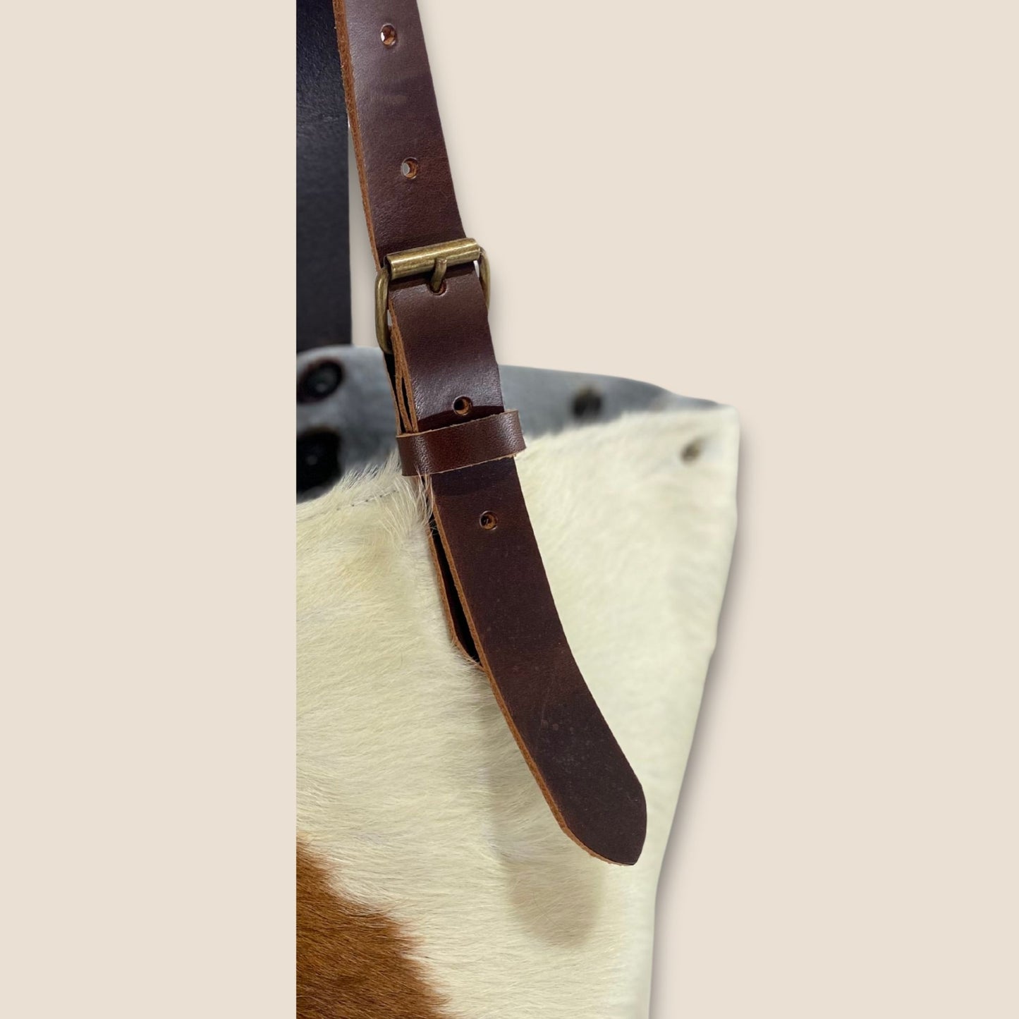 Gros plan sur la lanière réglable en cuir marron chocolat et sa boucle métallique, fixée sur le cabas en peau naturelle normande #13/147.