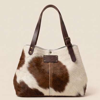 Cabas en peau de vache naturelle normande #13/147 présenté de face, avec coutures centrales, robe brune et blanche et anses en cuir chocolat.