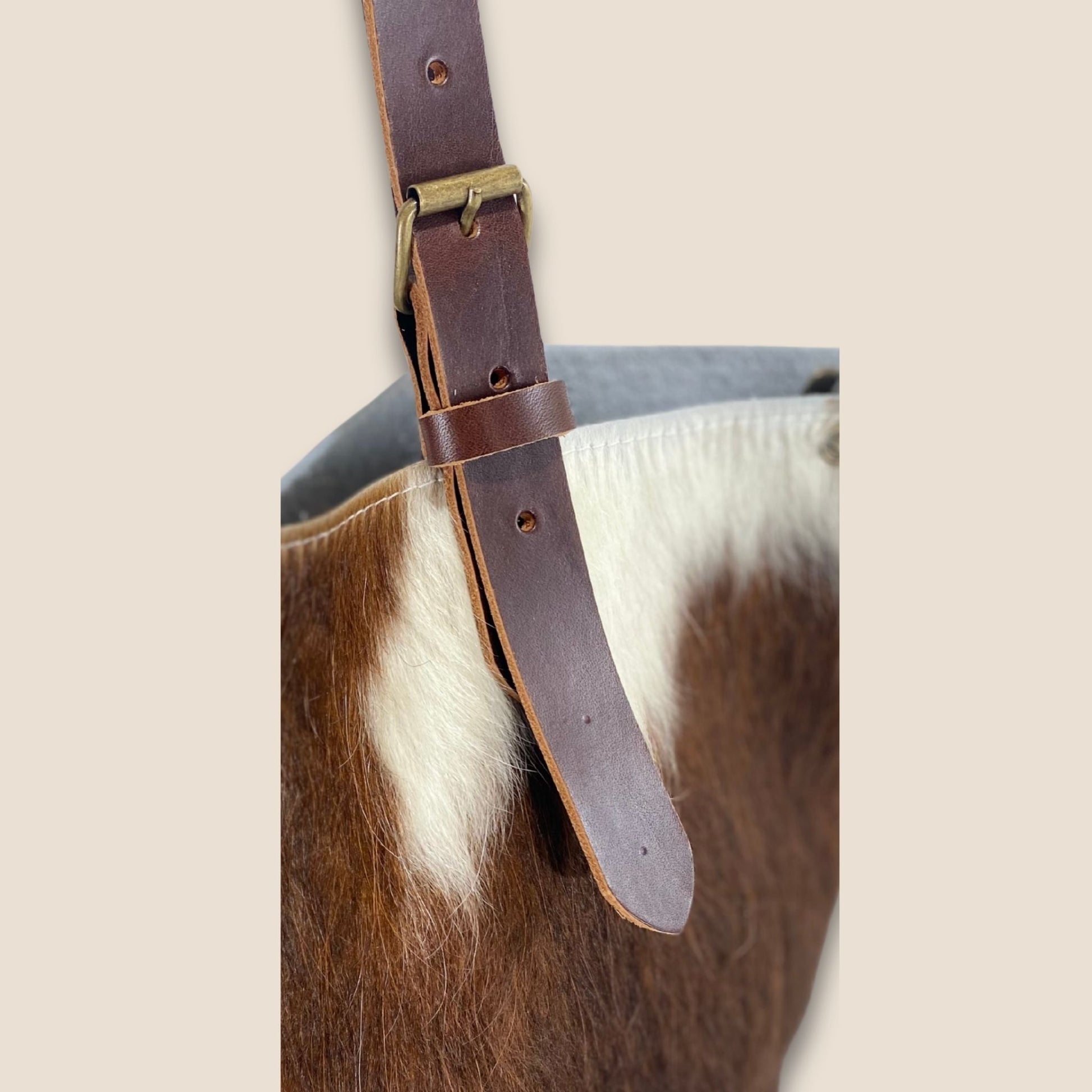 Gros plan sur la lanière réglable en cuir marron et sa boucle métallique, fixée sur le cabas en peau naturelle normande #13/146.